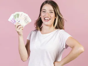 Tânără fată veselă, ţinând în mâna dreaptă un evantai de monede euro - Foto: Freepik/CC0