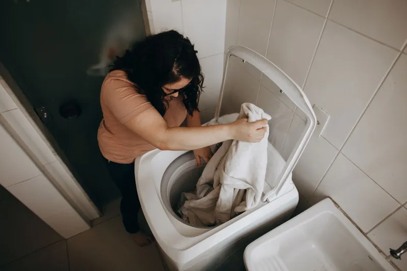 O femeie adultă &icirc;ncarcă haine &icirc;ntr-o mașină de spălat - Foto: Pexels (Imagine cu rol ilustrativ)