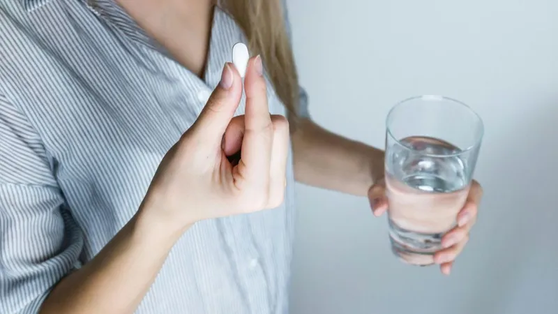 Femeie pregătindu-se să ia o pastilă, cu un pahar cu apă - Foto: Pexels/JES HOOTS