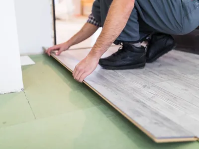 Muncitor care prelucrează o podea cu plăci laminate - Foto: Magnific.com (Imagine cu rol ilustrativ)
