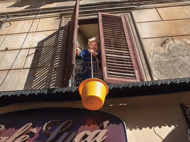 O femeie care locuiește deasupra unui restaurant, coboară o găleată în care a pus banii pentru comandă și așteaptă să primească mâncarea, în Palermo