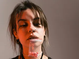 Femeie ţinând între dinţi un pacheţel de plastic cu pastile - Foto: Pexels/MART PRODUCTION