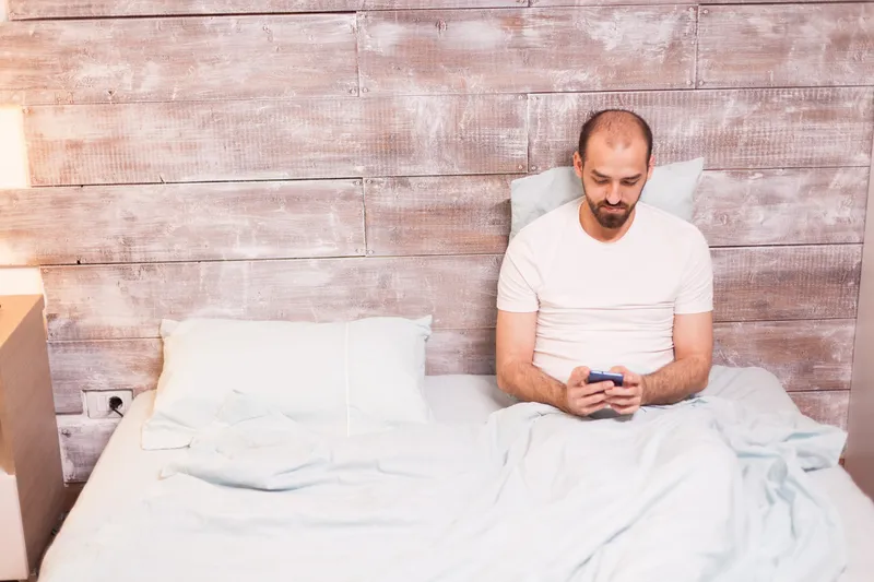 Bărbat relaxat noaptea, folosind telefonul mobil, st&acirc;nd &icirc;n pat - Foto: Magnific.com (Imagine cu rol ilustrativ)