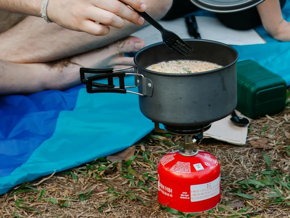 Cuplu la iarbă verde încălzindu-şi dejunul la o butelie autonomă de gaz - Foto: Pexels/Vanessa Garcia