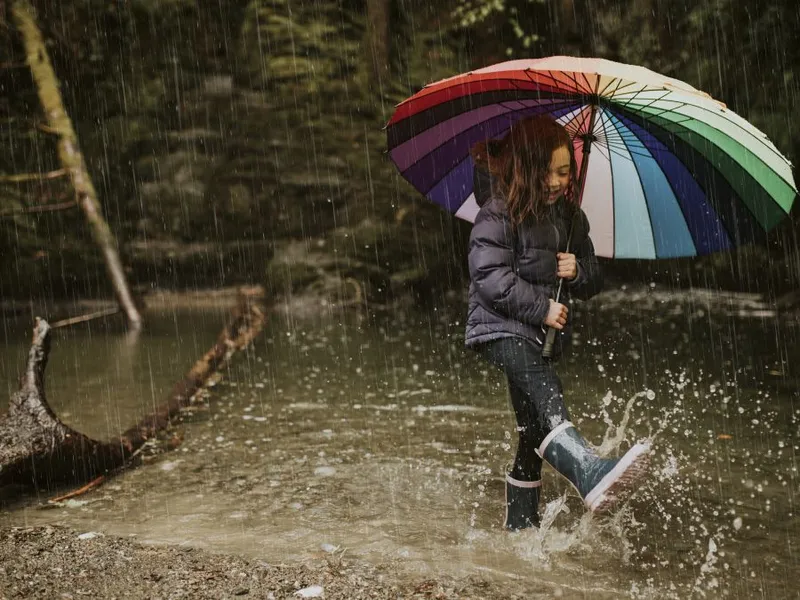 Fetiţă jucându-se în ploaie, cu cizme de cauciuc în picioare - Foto: Freepik/wirestock