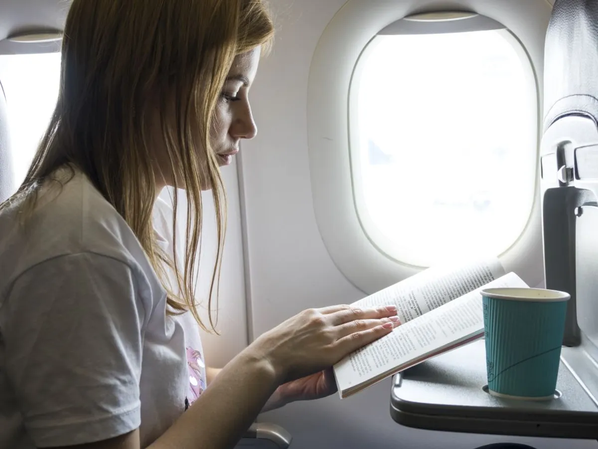 Femeie citind o carte, în avion - Foto: Magnific.com/freepik
