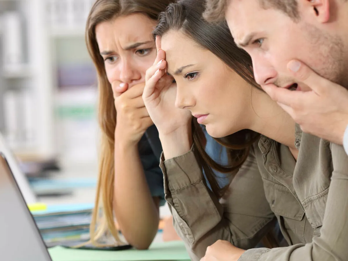 Trei persoane care se uită pe un laptop și se miră - Foto: Shutterstock