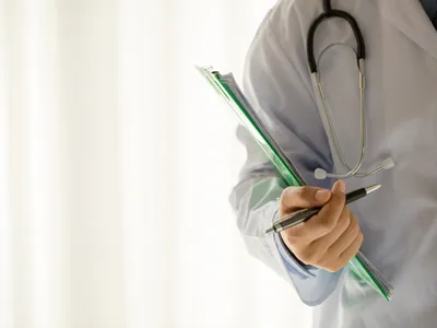 Doctor cu un dosar medical sub braţ şi stetoscop - Foto: Magnific.com/jcomp