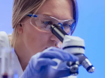 Femeie examinând o probă prin microscop - Foto: Pexels/Kindel Media