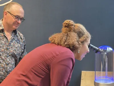 Autorul microsculpturii alături de o femeie care îi privește kucrarea prin microscop - Foto: Profimedia