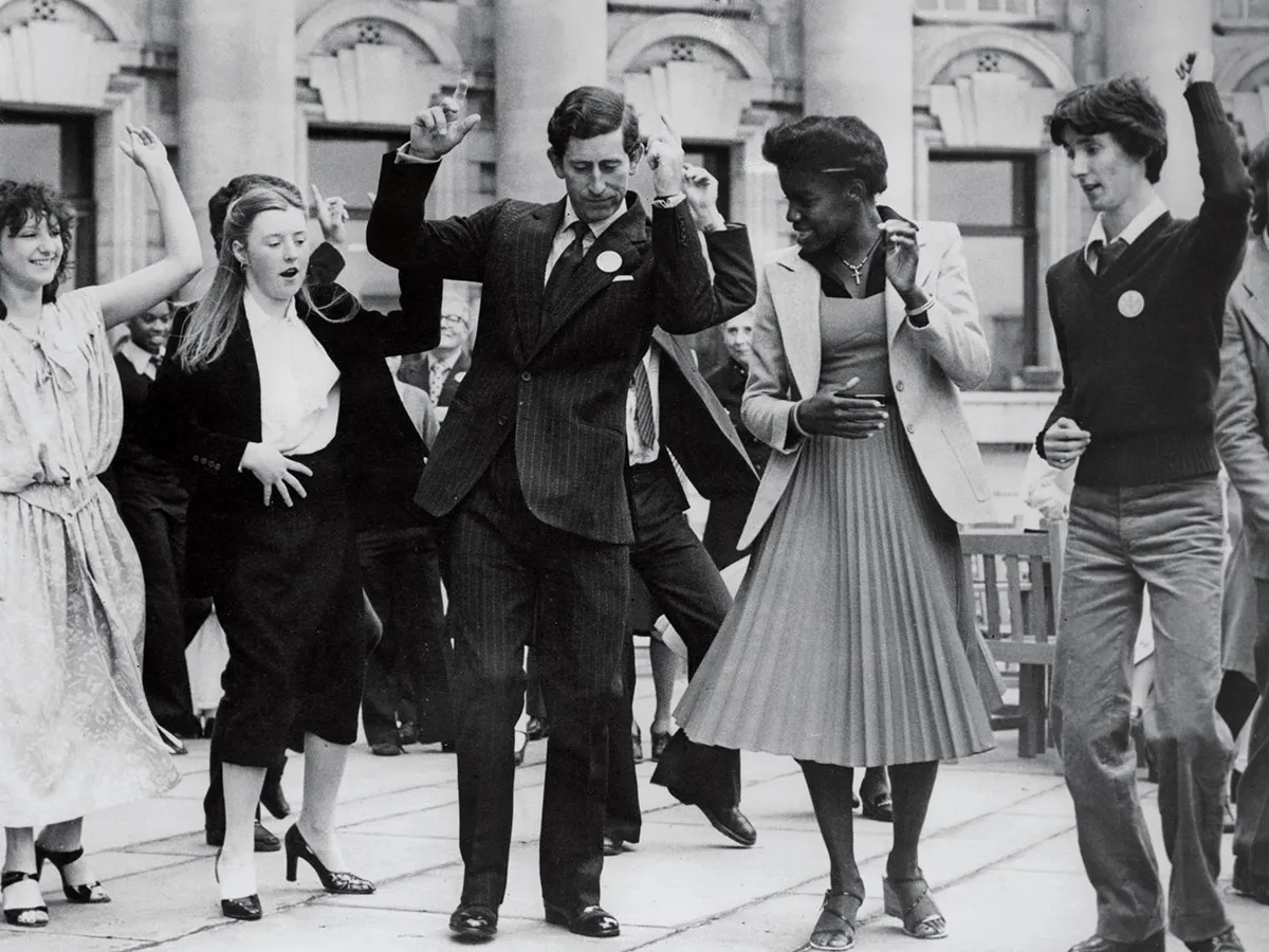 GĂSINDU-ȘI RITMUL În 1976, Charles a fondat The Prince’s Trust pentru a ajuta tinerii din medii defavorizate. Mai jos: Învățând un număr de dans în timp ce deschidea o expoziție culturală multietnică în centrul Londrei, în 1978