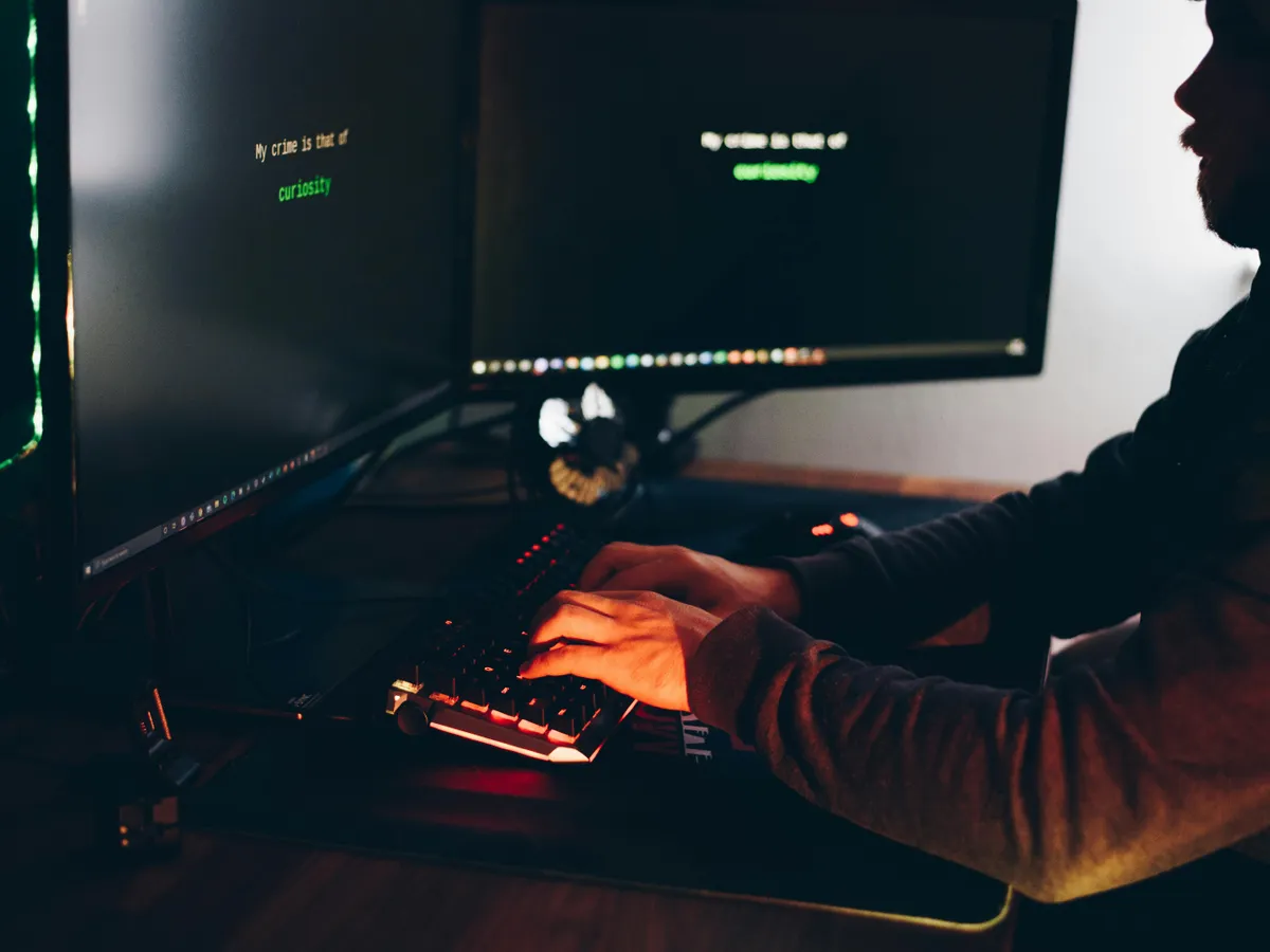 Silueta unui bărbat care scrie  la tastatură, în faţa a două monitoare - Foto: Pexels/Anete Lusina