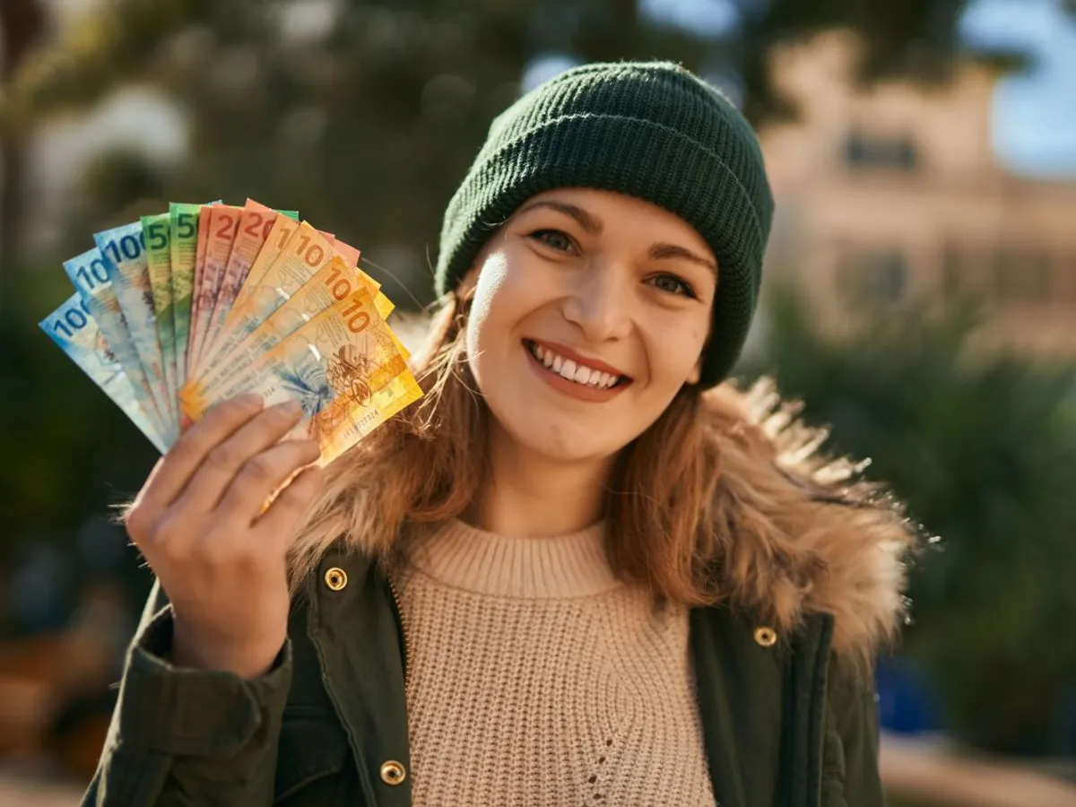 Femeie blondă veselă, cu un evantai de bancnote euro în mână - Foto: Magnific.com/krakenimages.com