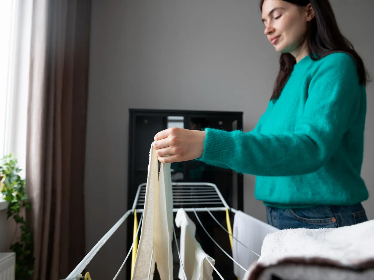 Femeie care strânge haine de pe suport - Foto: Freepik (Imagine cu rol ilustrativ)