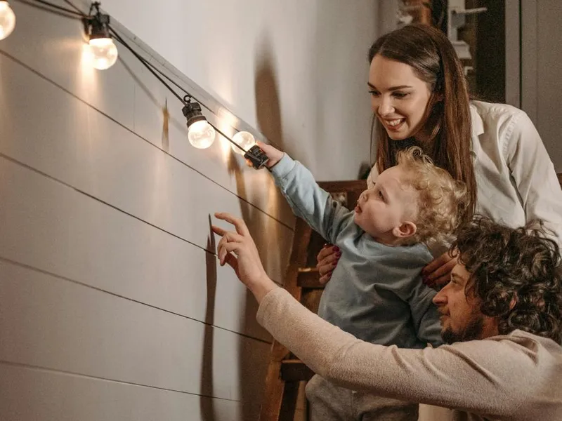 Tânără familie cu copil admirând aranjamentele cu lumini, în afar casei - Foto: Pexels/Pavel Danilyuk
