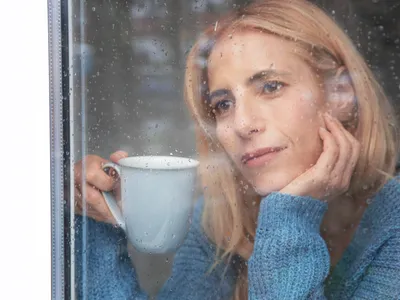 Femeie matură care se uită pe fereastră în timp ce plouă - Foto: Magnific.com (Imagine cu rol ilustrativ)