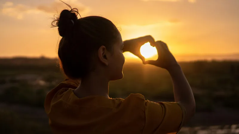 Femeie în concediu făcând semnul inimii în soare - Foto: Pexels/Hassan OUAJBIR