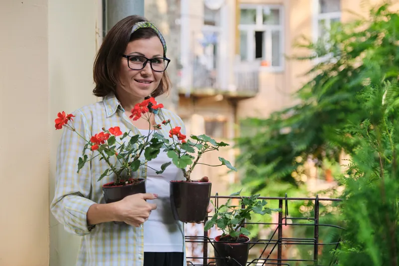 Femeie cu flori &icirc;n balcon - Foto: Magnific.com (Imagine cu rol ilustrativ)