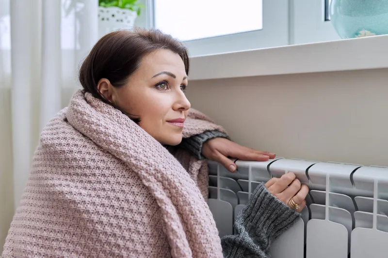 Femeie care stă așezată lângă un calorifer - Foto: Freepik (rol ilustrativ)