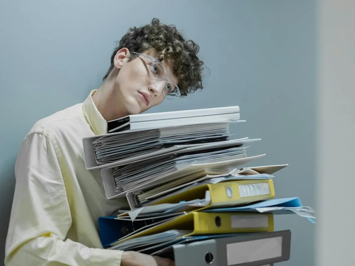 Tânăr în cămaşă galbenă ducând în braţe mai multe bibliorafturi de documente - Foto: Pexels/cottonbro studio