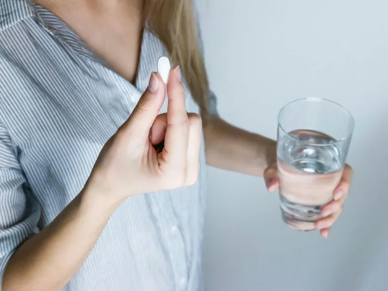 Femeie pregătindu-se să ia o pastilă, cu un pahar cu apă - Foto: Pexels/JES HOOTS