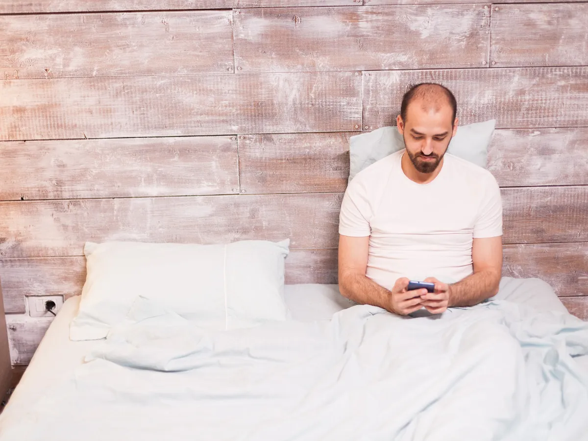 Bărbat relaxat noaptea, folosind telefonul mobil, stând în pat - Foto: Magnific.com (Imagine cu rol ilustrativ)