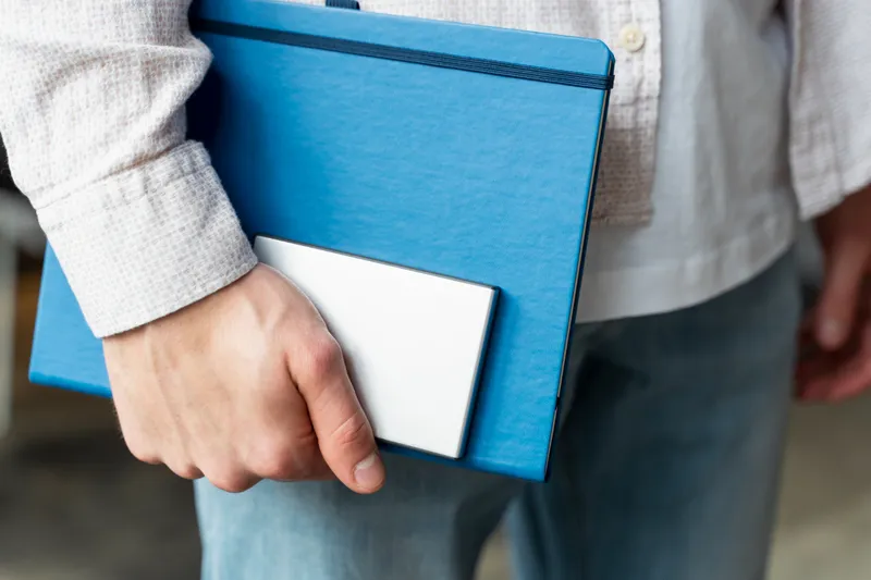 Prim-plan m&acirc;nă țin&acirc;nd SSD și notebook - Foto: Magnific.com (Imagine cu rol ilustrativ)