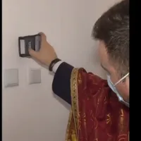 Un preot sfințește o casă cu ștampila