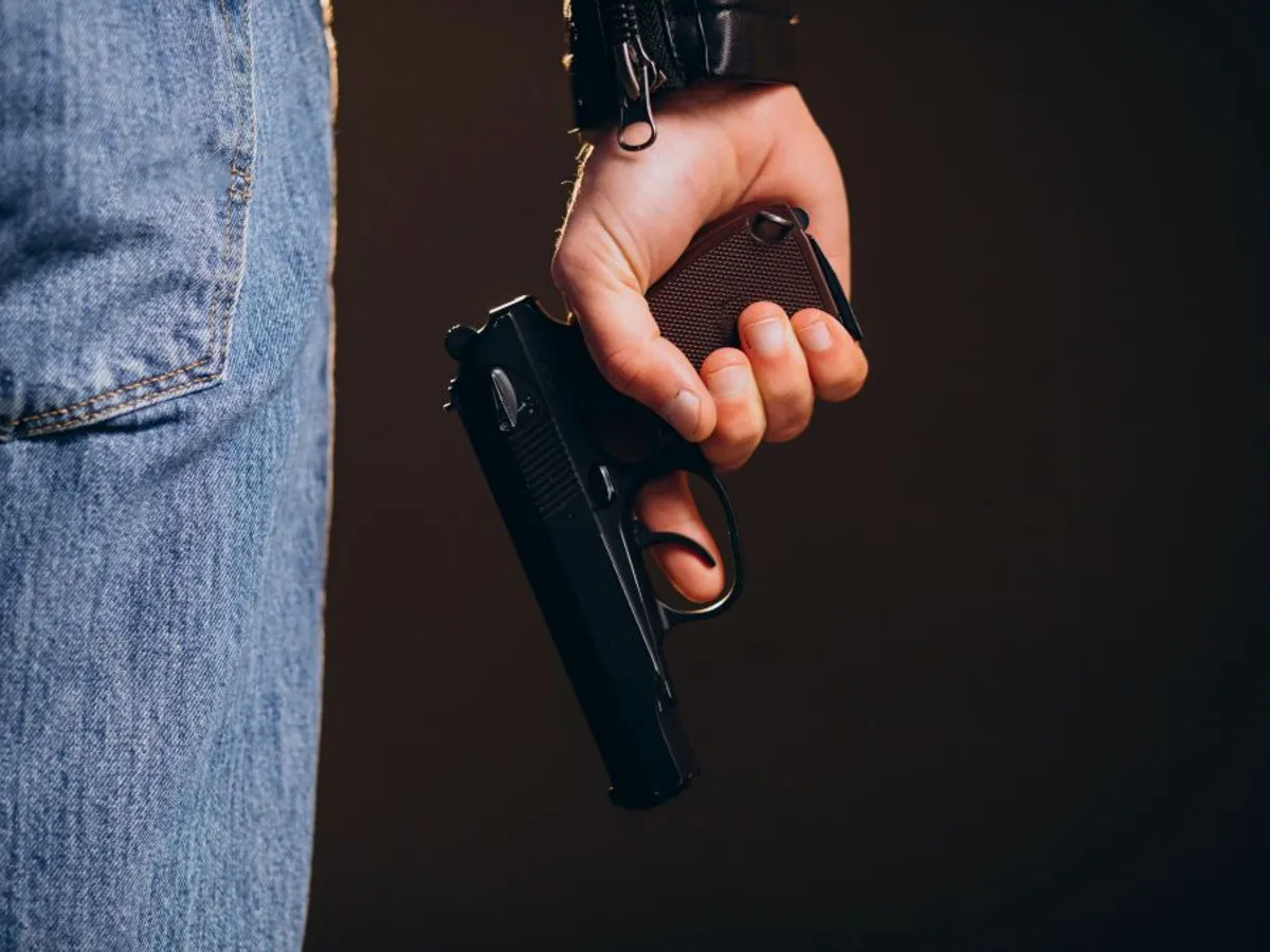 Bărbat îmbrăcat în blugi ţinând în mână un pistol - Foto: Freepik/senivpetro