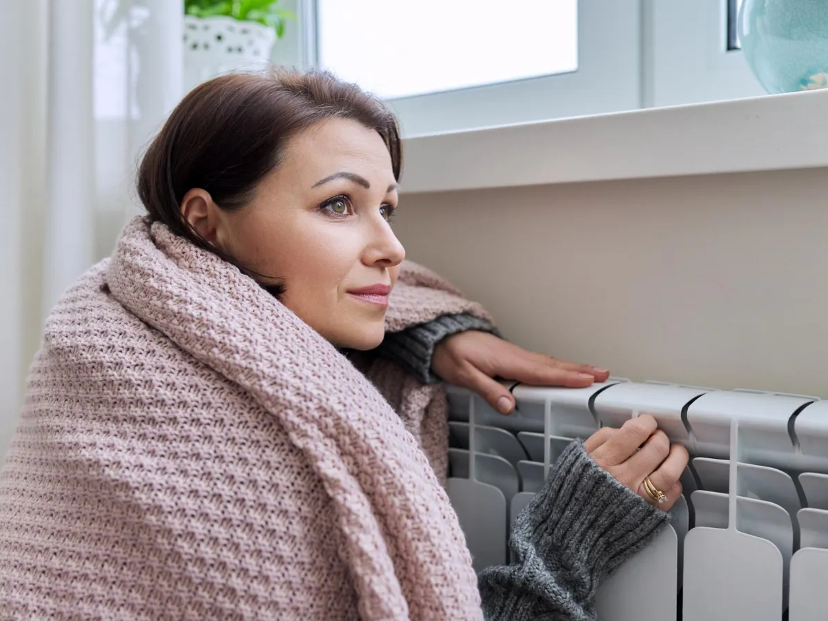 Femeie care stă așezată lângă un calorifer - Foto: Freepik (rol ilustrativ)