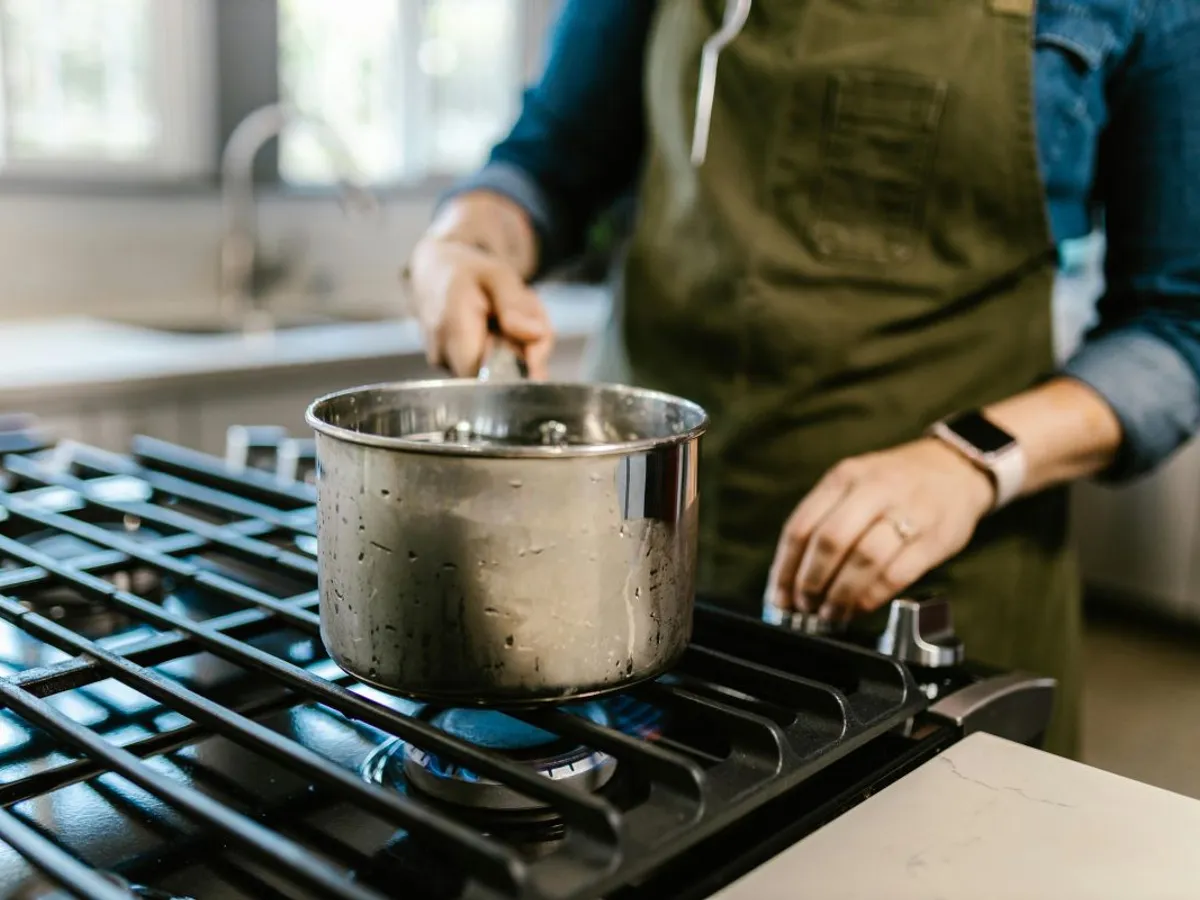 Femeie pregătind mâncarea, pe aragaz, în oală - Foto: Pexels/RDNE Stock project