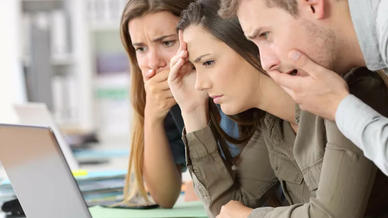 Trei persoane care se uită pe un laptop și se miră - Foto: Shutterstock