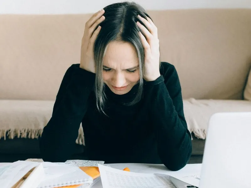 Femeie obosită ţinându-şi capul în mâini de atâtea calcule - Foto: Pexels/Nataliya Vaitkevich