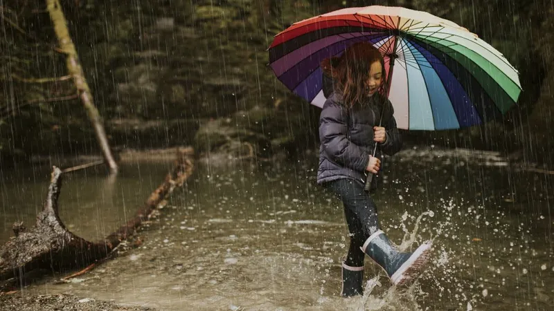 Fetiţă jucându-se în ploaie, cu cizme de cauciuc în picioare - Foto: Freepik/wirestock
