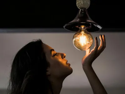 Femeie admirând un bec cu filament - Foto: Pexels/Victor Miyata