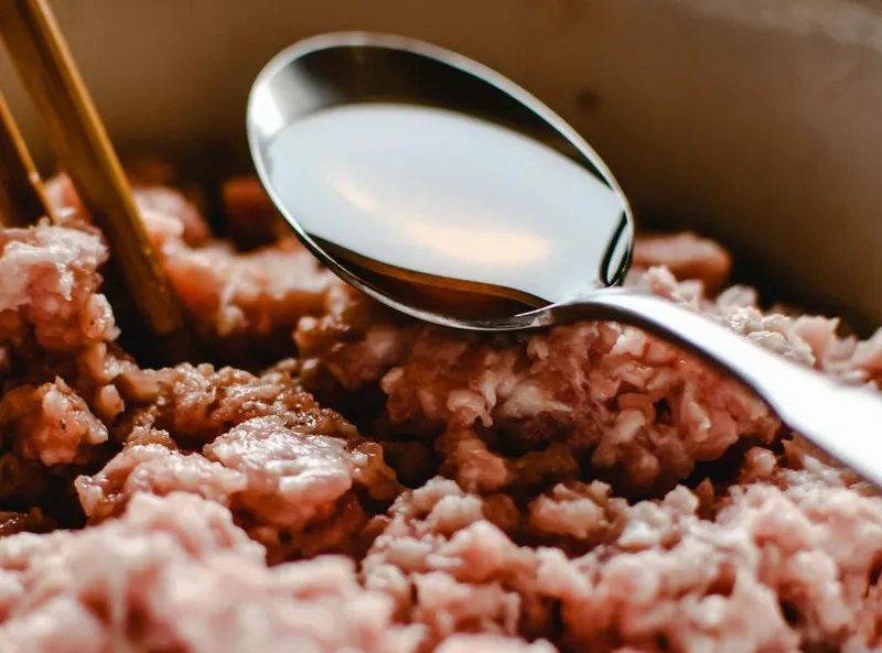 Lingură din oţel inoxidabil cu ulei în ea, deasupra cărnii tocate de porc - Foto: Pexels-Eva Bronzini