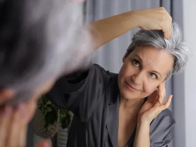Femeie cu părul grizonat care se uită în oglindă - Foto: Freepik (Imagine cu rol ilustrativ)