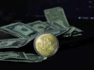 Cash pe o masă, împreună cu o monedă bitcoin - Foto: Pexels/beyzahzah