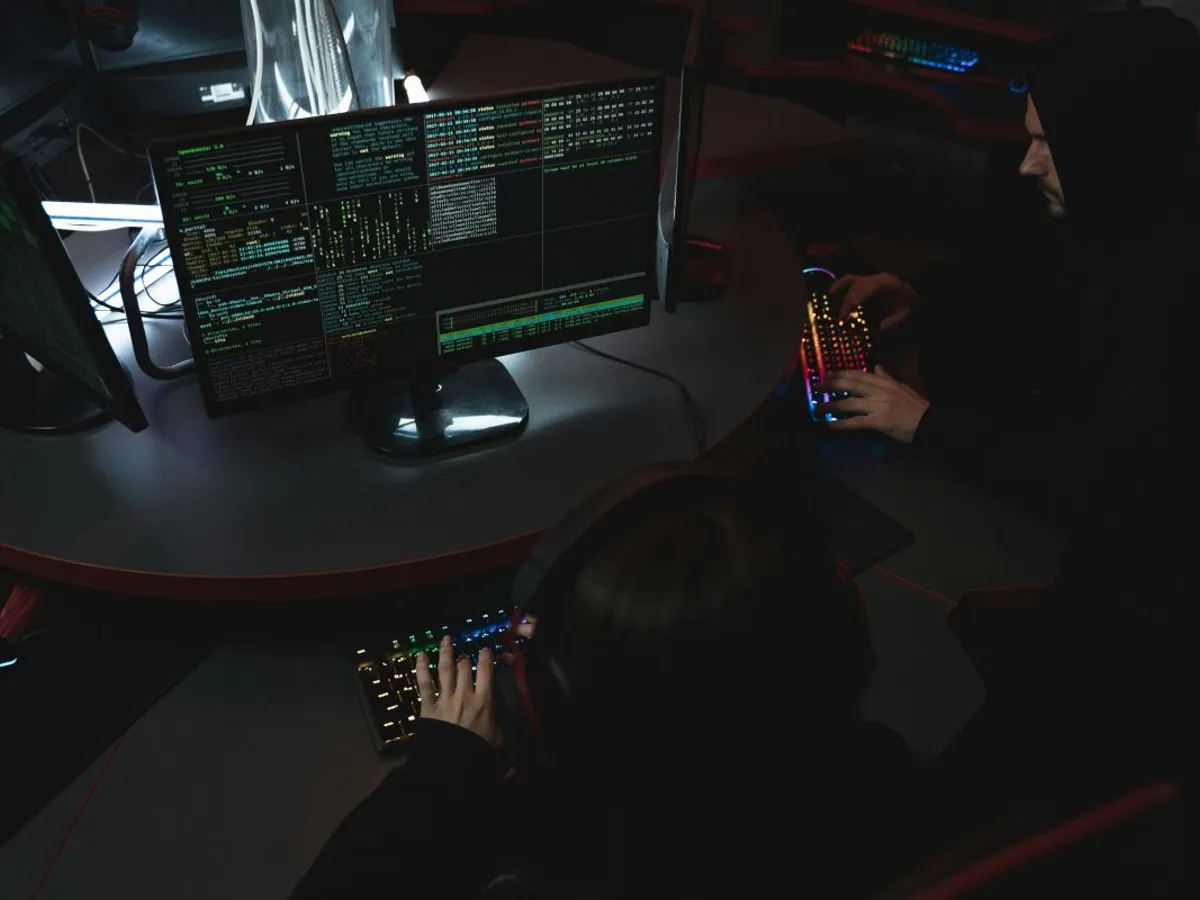 Doi tineri folosind computere, în clarobscur - Foto: Pexels/Tima Miroshnichenko