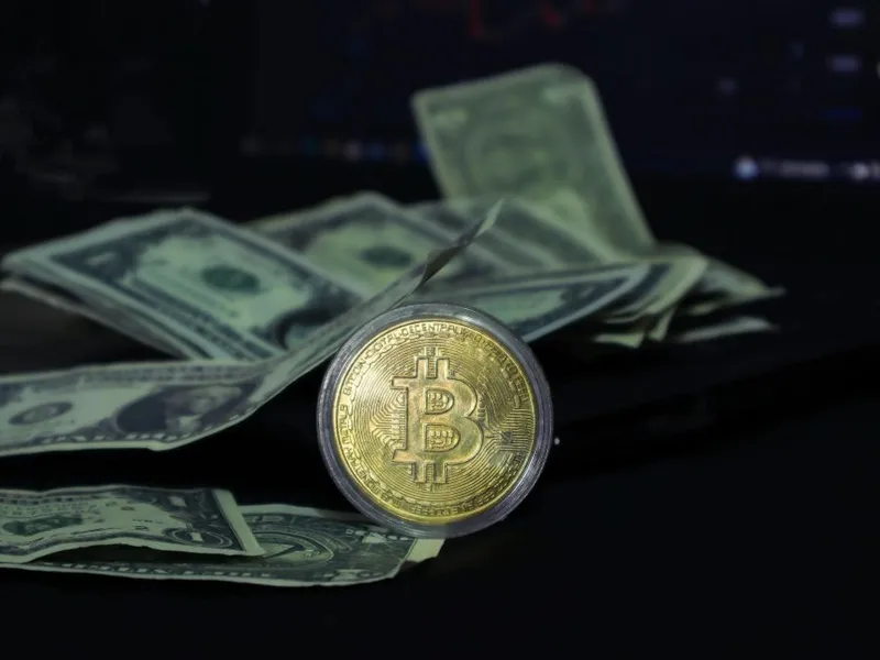 Cash pe o masă, împreună cu o monedă bitcoin - Foto: Pexels/beyzahzah
