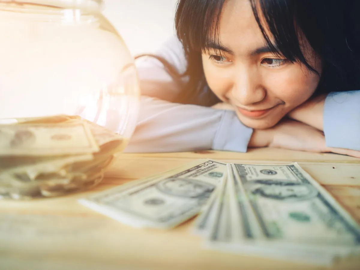 Prim-plan al unei femei zâmbitoare cu bancnote pe masă - Foto: Freepik (rol ilustrativ)