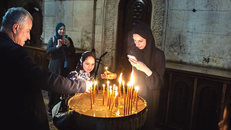 Palestinienii musulmani Mohammad Musa (stânga), Dareen Layla (spate), Lubna Musa (centru) și Eleen Musa (dreapta) aprind lumânări în interior biserica Sfântul Mormânt din Ierusalim (15 aprilie 2022)