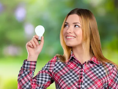 Femeie zâmbind cu un bec ecologic în mână - Foto: Freepik/fabrikasimf