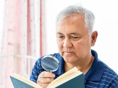 Bărbat chinez care se uită cu lupa într-o carte - Foto: Freepik (rol ilustrativ)