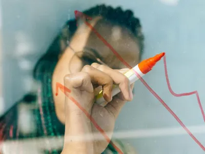 Femeie desenând un grafic, pe un panou transparent - Foto: Pexels/Nataliya Vaitkevich