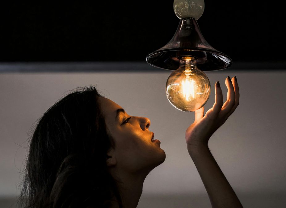 Femeie admirând un bec cu filament - Foto: Pexels/Victor Miyata